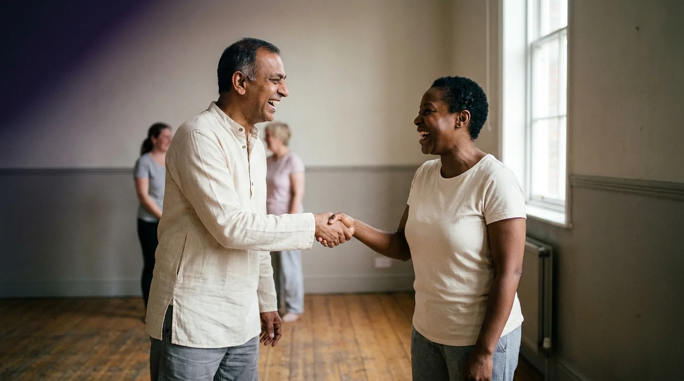Two practitioners face-to-face in the greeting-laugh exercise of laughter yoga, hands meeting at a mock handshake mid-laugh