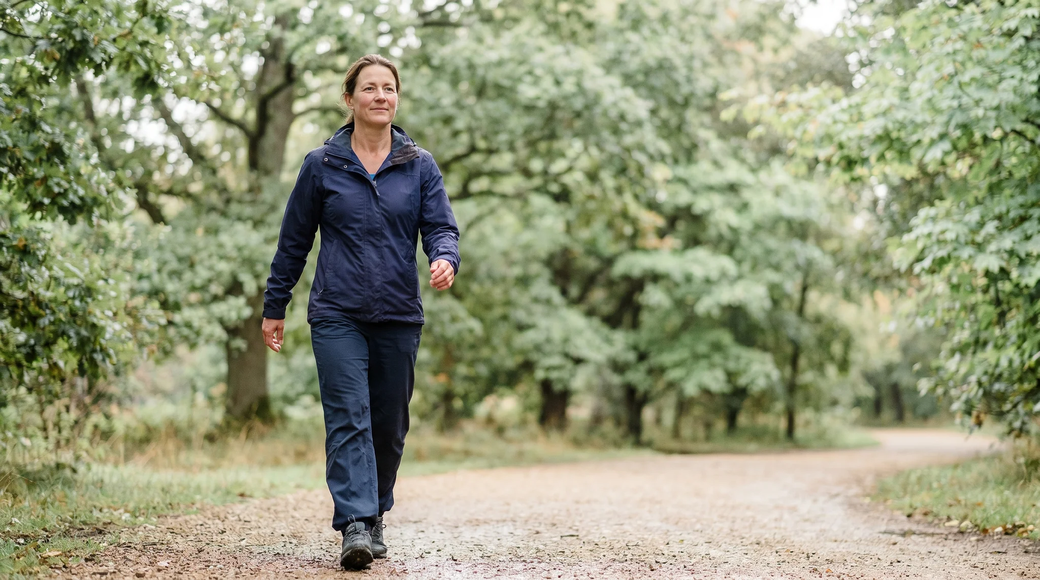Woman with a fuller build taking a brisk low impact exercise walk on a sunlit tree-lined path