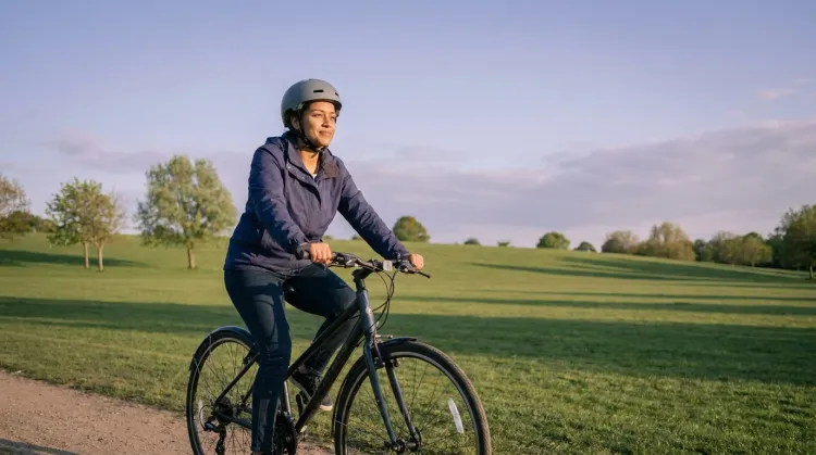 Everyday woman cycling for mental health on an upright bike through open golden-hour parkland, calm expression