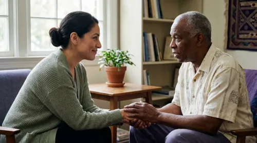 Clinician leaning in to listen, a reassuring hand on an older patient's hands during a patient-centered care visit