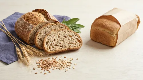 A nutritious whole-grain loaf with wheat stalks and grains beside a plainly-packaged gluten-free bread on a wood surface