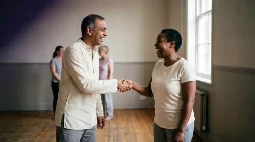 Two practitioners face-to-face in the greeting-laugh exercise of laughter yoga, hands meeting at a mock handshake mid-laugh