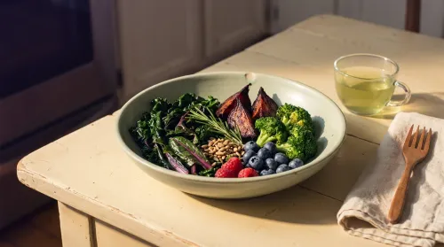 Epigenetic-diet bowl with dark leafy greens, roasted beets, broccoli, and blueberries on a wood table in late-afternoon light